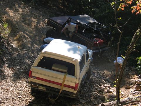 1995 Ford Bronco - Two off-road vehicles navigate a challenging dirt path, with one vehicle appearing to be a 1995 Ford Bronco.