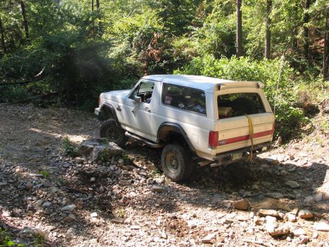 1995 Ford Bronco - A white Ford Bronco navigates a challenging rocky trail through a wooded area.