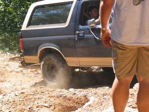 1995 Ford Bronco - A 1995 Ford Bronco navigates a rocky, off-road trail, with its rear tire kicking up dust.