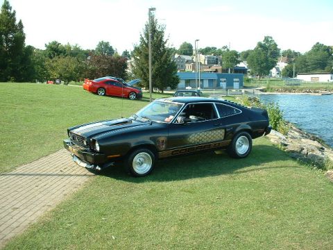 1978 Ford Mustang II - A black 1978 Ford Mustang II Cobra II is parked by the water, with another car visible in the background.