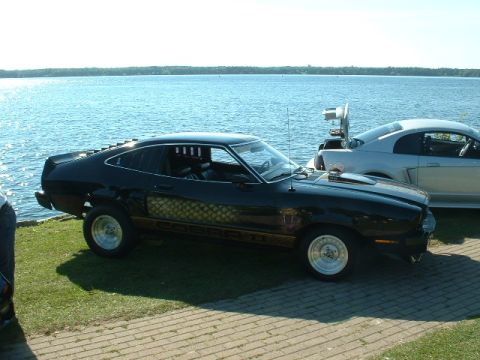 1978 Ford Mustang II - A black 1978 Ford Mustang II Cobra II is parked by a lake, with another car visible behind it.