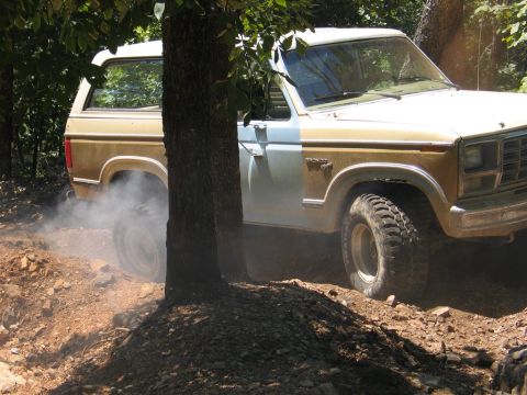 1995 Ford Bronco - This Ford Bronco is navigating a rough, wooded terrain, with dust and smoke billowing from its rear tire.