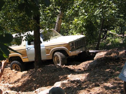 1995 Ford Bronco - A Ford Bronco navigates a challenging off-road course surrounded by dense foliage.