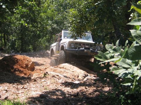 1995 Ford Bronco - First-gen Ford Bronco tackles an off-road obstacle on a sunny day.
