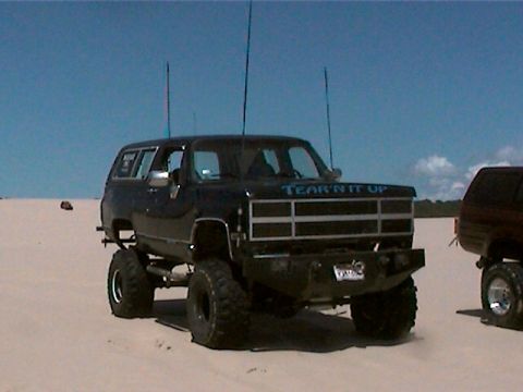 1977 Ford F-150 - This lifted black SUV is parked on sand, with another vehicle visible to the right.