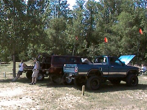 1977 Ford F-150 - A blue pickup truck with a lifted suspension and its hood open is parked next to other vehicles under trees.