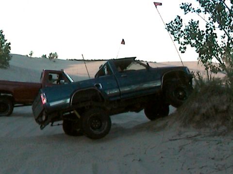 1977 Ford F-150 - Two pickup trucks are seen on a sand dune, with one truck angled on the dune's crest.
