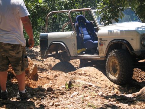 1995 Ford Bronco - This classic Ford Bronco is tackling a challenging off-road course with a person standing nearby.