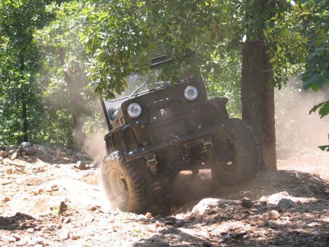 1995 Ford Bronco - An off-road vehicle kicks up dust as it maneuvers through a challenging, wooded terrain.