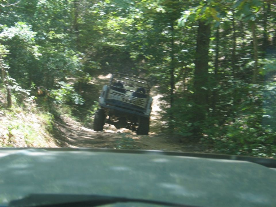 Off-road vehicle driving on a wooded trail, seen from behind