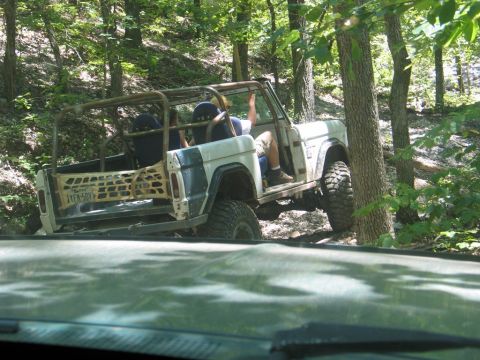 1995 Ford Bronco - A modified Ford Bronco navigates a challenging off-road path through a dense forest.