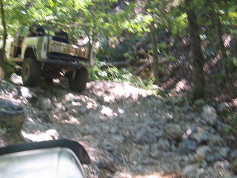 1995 Ford Bronco - An off-road vehicle navigates a challenging, rocky trail through a wooded area.