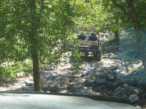 1995 Ford Bronco - An off-road vehicle navigates a challenging rocky trail surrounded by dense trees.