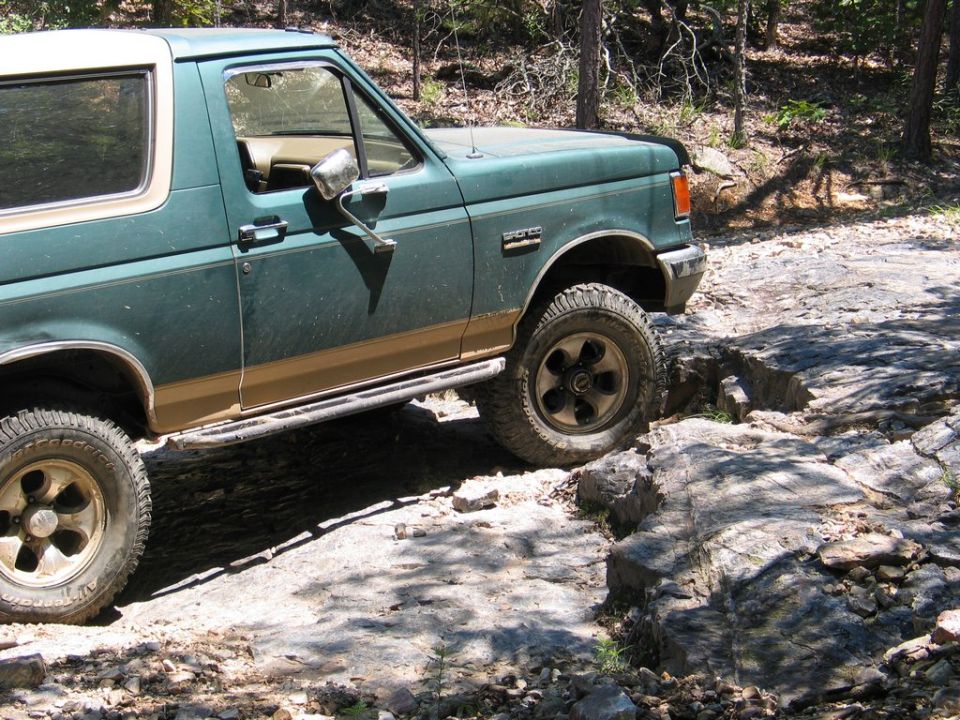 Green Ford Bronco driving over rocks on a trail