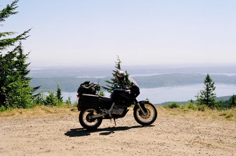 1997 BMW F650 - A 1997 BMW F650 motorcycle is parked on a dirt road, offering a view of a distant body of water and forested hills.