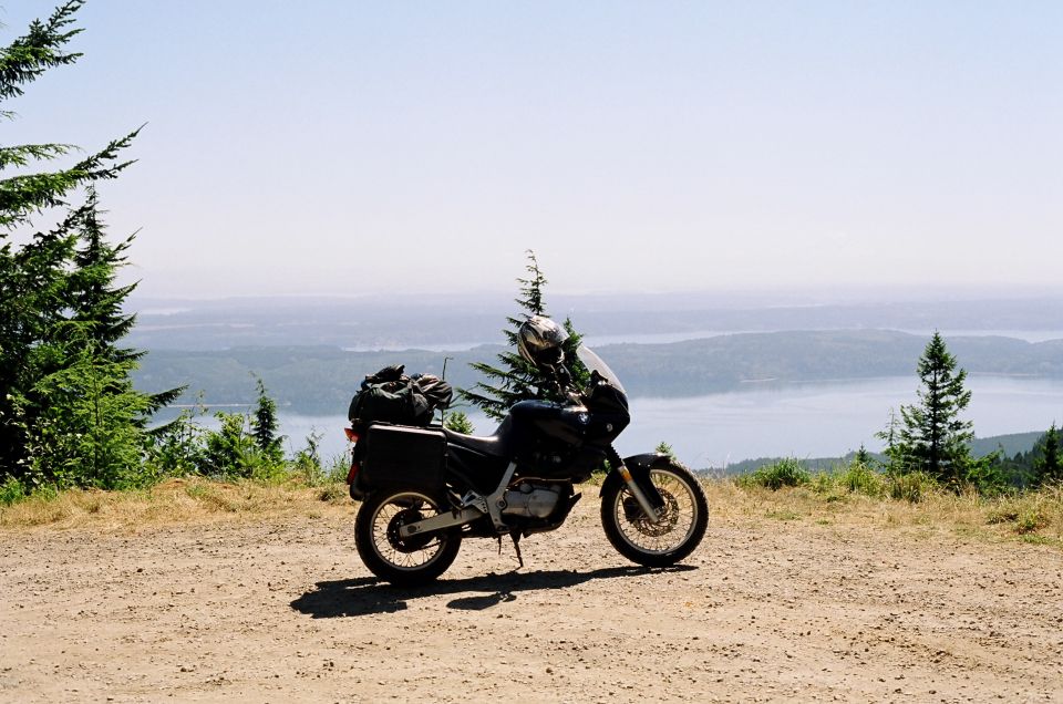 Black BMW dual-sport motorcycle parked on dirt overlook above hazy lake and hills