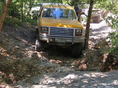 1995 Ford Bronco - An off-road vehicle navigates a steep, rocky incline on a wooded trail.