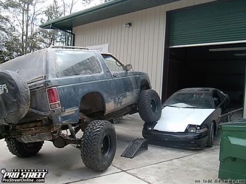 1992 Chevrolet S10 - A lifted 1992 Chevrolet S10 Blazer is parked next to another car in front of a garage.