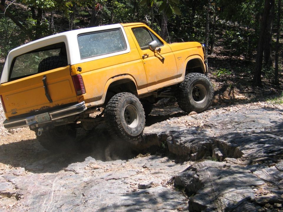 Yellow SUV with white top driving over rocks on a trail. It has large off-road tires and a spare tire mounted inside