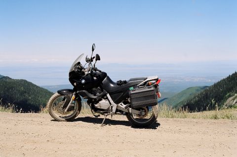 1997 BMW F650 - A black BMW motorcycle is parked on a dirt road overlooking a vast mountain landscape under a clear blue sky.
