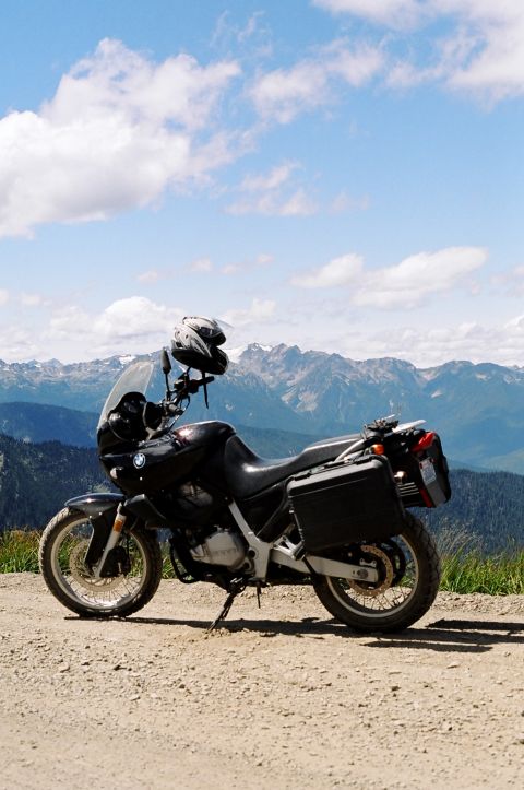 1997 BMW F650 - A black motorcycle with saddlebags is parked on a dirt road with a scenic mountain range behind it.