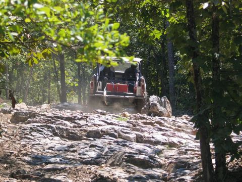 1995 Ford Bronco - Vehicle tackling a challenging rocky path through a forest during an off-road event.