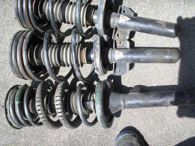 Three used MacPherson strut and coil spring assemblies laid out on asphalt