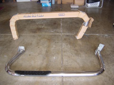1990 Ford Bronco - A pair of chrome side steps for a vehicle are shown in their packaging on a concrete floor.