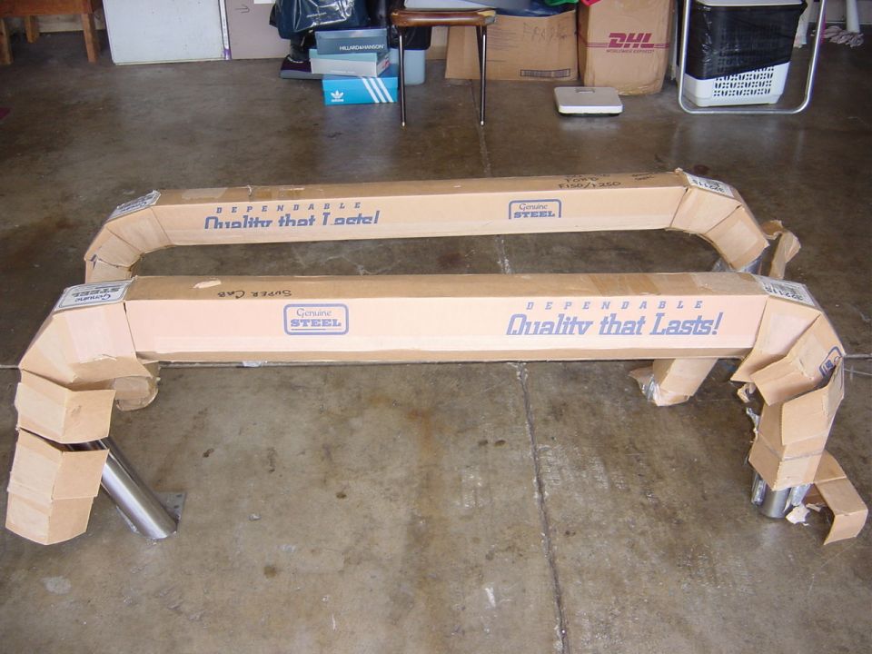 Two boxed car parts, possibly running boards, on a concrete floor. Text on boxes reads 'DEPENDABLE Quality that Lasts!' and 'Genuine STEEL'