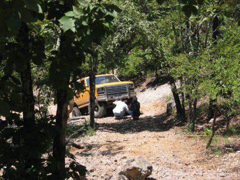 1995 Ford Bronco - Two people inspect the front of a yellow pickup truck on an off-road trail.
