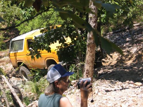 1995 Ford Bronco - A person films a yellow SUV navigating a rough, wooded trail.