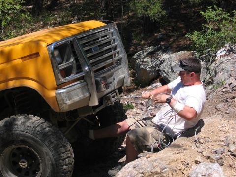 1995 Ford Bronco - Man winching a yellow off-road vehicle out of a difficult spot on a trail.