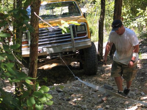 1995 Ford Bronco - A man walks near a yellow Ford Bronco that appears to be stuck on a rough, wooded trail.