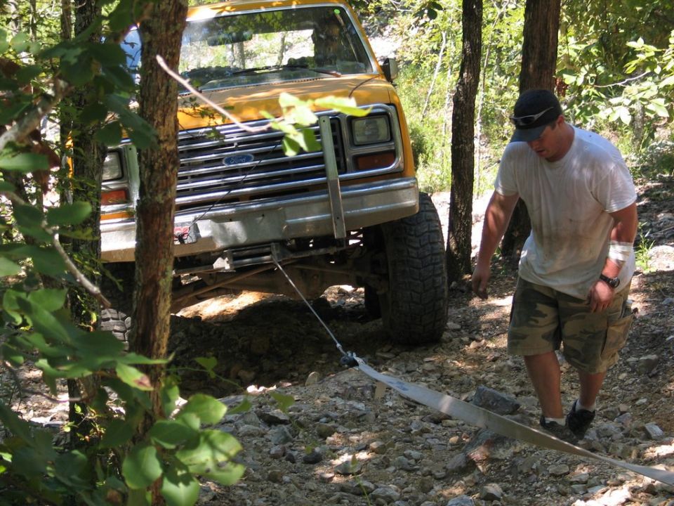 Yellow Ford Bronco, possibly from the early 80s, is stuck on a rocky trail with a man walking nearby