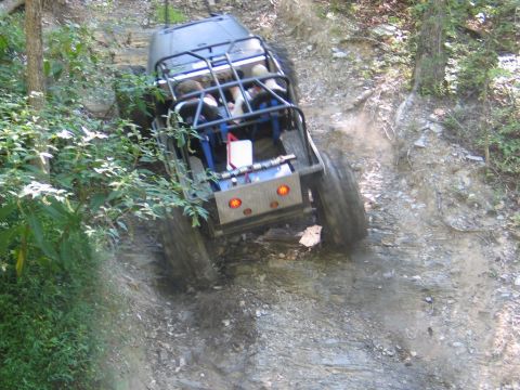 1995 Ford Bronco - An off-road vehicle navigates a steep, rocky incline with dense foliage on the left.