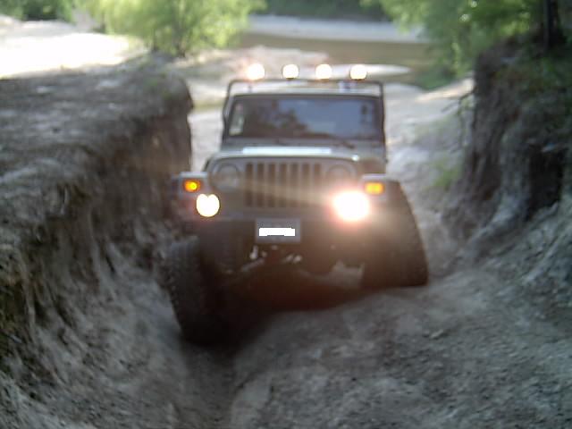 Front of a Jeep Wrangler with lit headlights and roof lights crawling a deep blurry sand rut