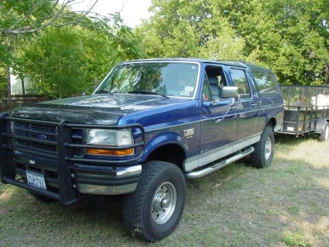 1994 Ford C-350 (Centurion Conversions) - Blue Ford Bronco Centurion with a trailer is parked on grass.