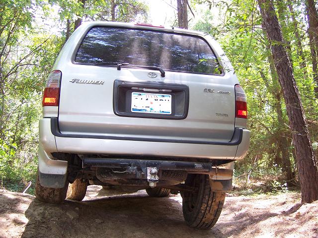 Rear of silver Toyota 4Runner with Toyota badge climbing a rocky ledge in shaded woods
