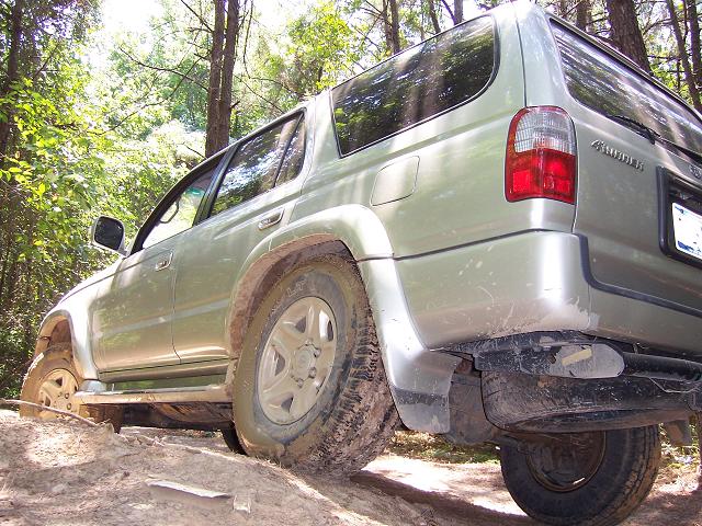 Low rear-quarter view of silver Toyota 4Runner flexed over rocks in green forest
