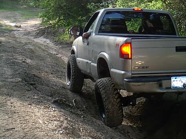 Lifted tan Chevrolet S-10 on mud tires climbing a dirt embankment