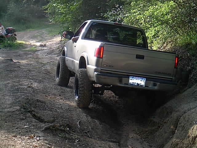 Lifted tan Chevrolet pickup descending a rutted dirt trail tractor in background