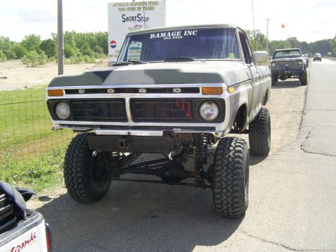 1977 Ford F-150 - A lifted 1977 Ford F-150 truck is parked on the side of the road, with another truck visible in the background.