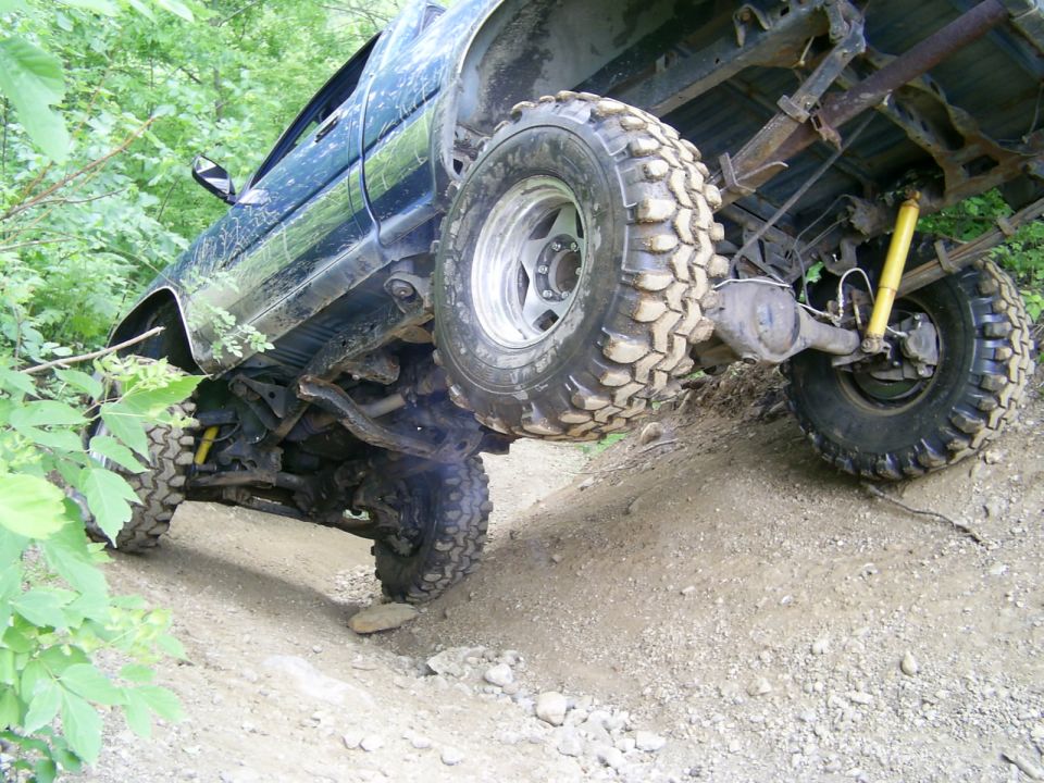 Off-road truck with large tires climbing a dirt hill, showing suspension and rear axle