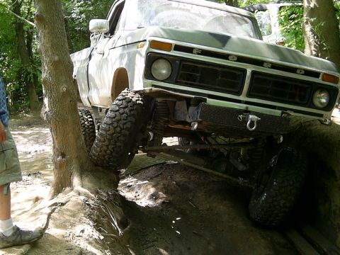 1977 Ford F-150 - A lifted 1977 Ford F-150 navigates a challenging off-road course, with one tire on a tree root.