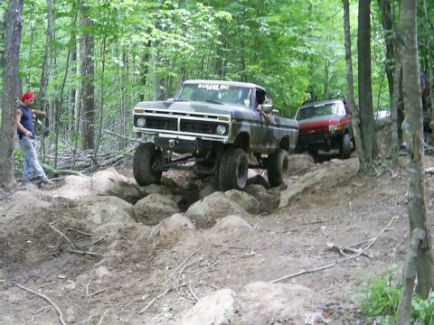 1977 Ford F-150 - Two trucks navigate a challenging rocky trail in a wooded area.
