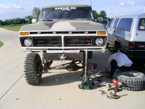 1977 Ford F-150 - A person works on the front end of a lifted 1977 Ford F-150, which is supported by a jack.
