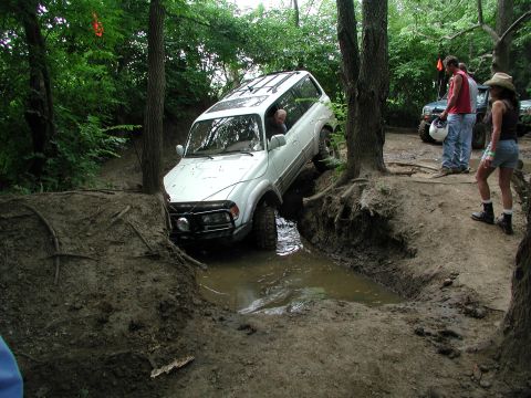 1977 Ford F-150 - This white SUV is navigating a challenging muddy trail with water and uneven terrain.