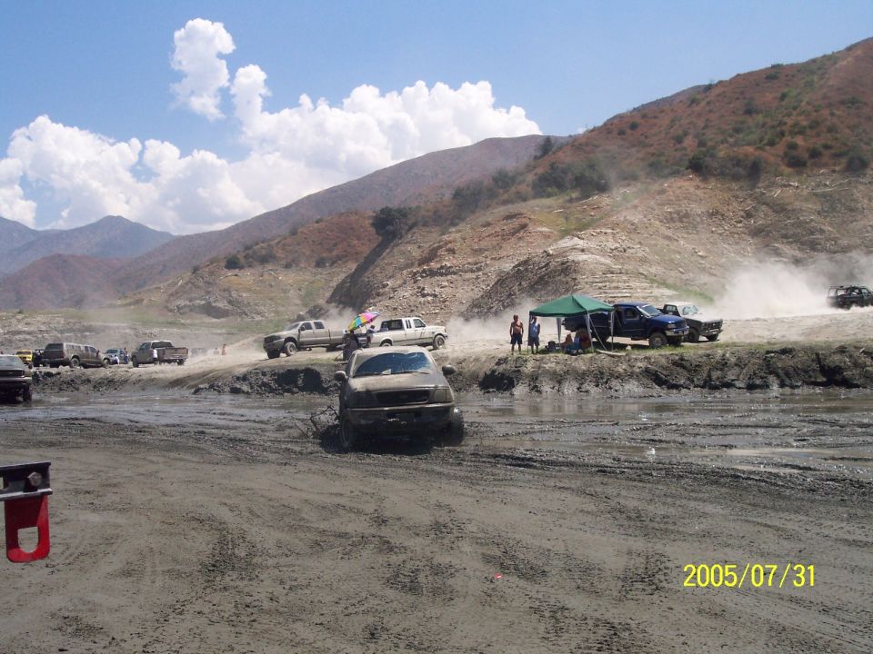Trucks driving through mud with people watching and tents set up