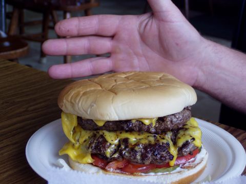1983 Ford Bronco - A large double cheeseburger is presented on a paper plate, with a hand hovering above it.