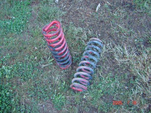 1993 Ford Bronco - Two used coil springs, one red and black, the other blue and red, are shown on a grassy surface.